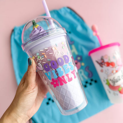 Hand holding a colorful tumbler with 'Good Vibes Only' text against a pink background