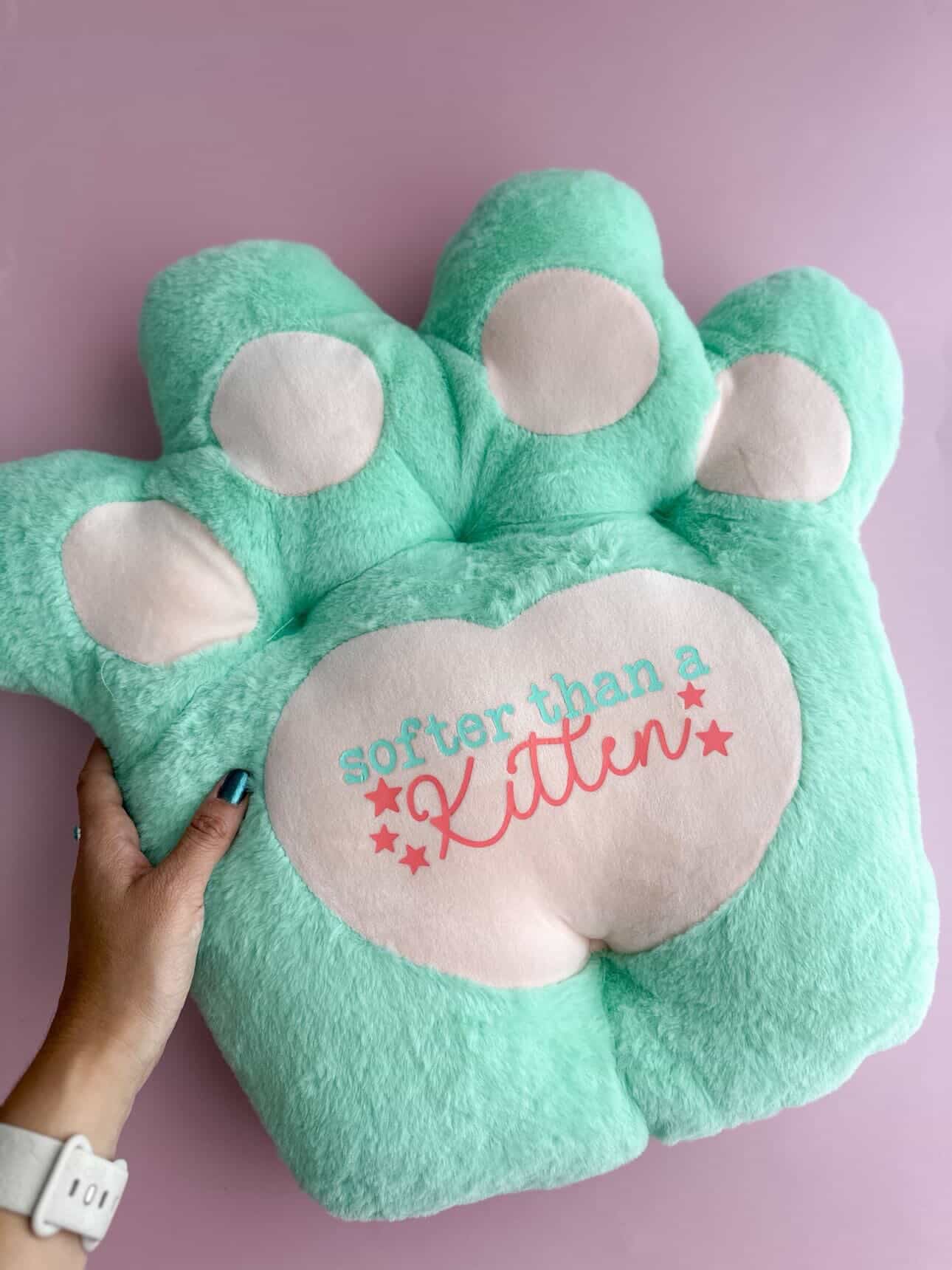 Green paw-shaped pillow with 'softer than a kitten' text on a pink background