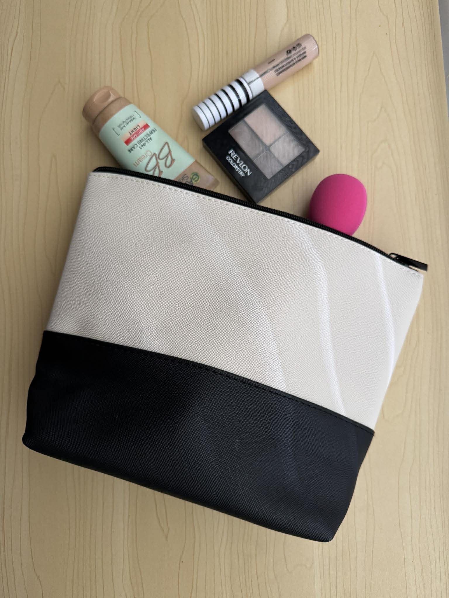 Black and white makeup pouch with cosmetic items on a wooden surface
