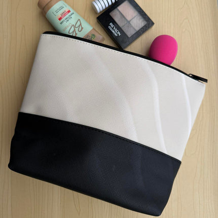 Black and white makeup pouch with cosmetic items on a wooden surface